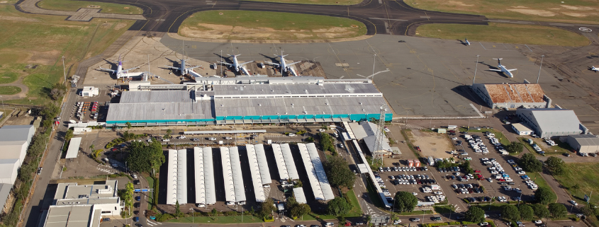 Aerial view of Townsville Airport terminal with parked aircraft, parking lots, and surrounding runways and taxiways.