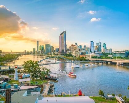 Picture of Brisbane city skyline and Brisbane River at twilight. Partly cloudy sky with a ferry in the river below. 