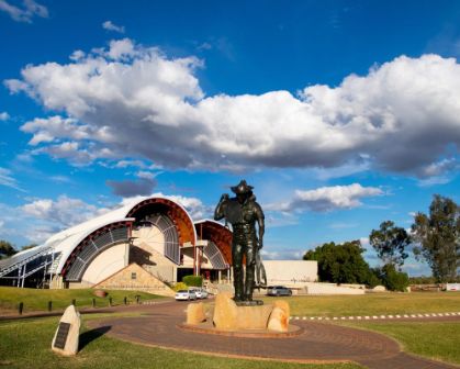 Picture of Bronze statue of a stockman in front of the Australian Stockman’s Hall of Fame under a blue sky with scattered clouds, Longreach.