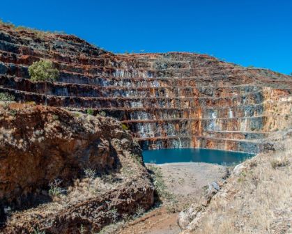 Picture of An open pit mine with terraced rock layers in varied colors and a small body of water at the bottom, surrounded by dry, rocky terrain.