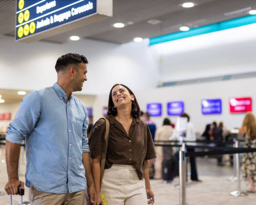 Two travelers walk through Townsville Airport terminal toward check-in counters, with directional signage for Departures and Arrivals visible overhead.