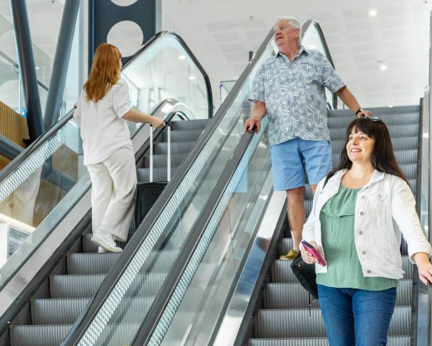 Passengers on escalators inside Townsville Airport, one with suitcase ascending and two descending.