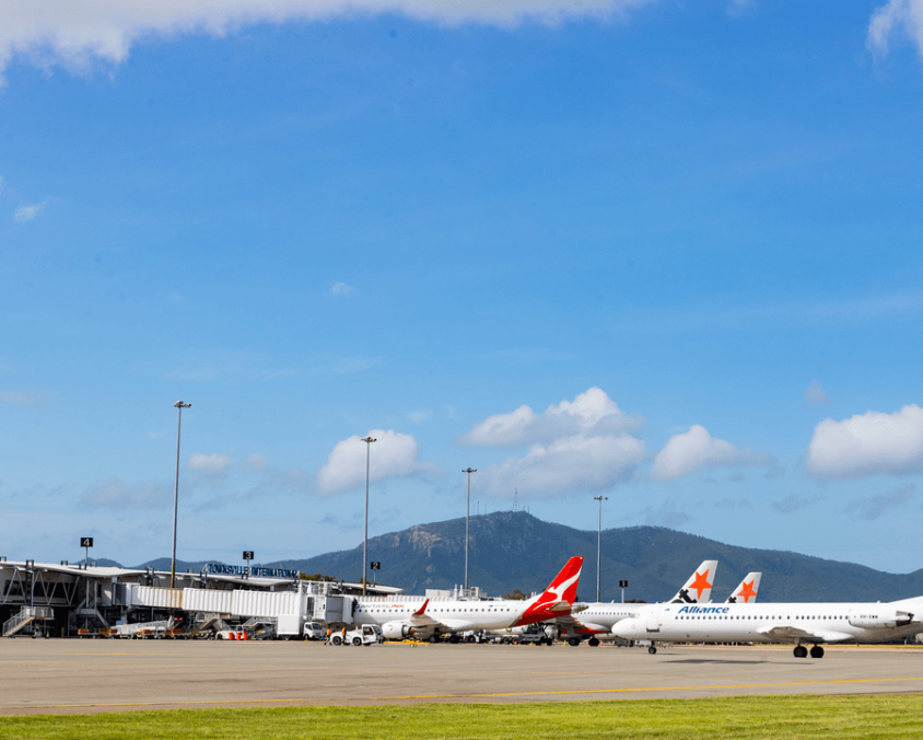 Townsville Airport tarmac with Qantas and Alliance aircraft at gates, terminal and mountains in background.